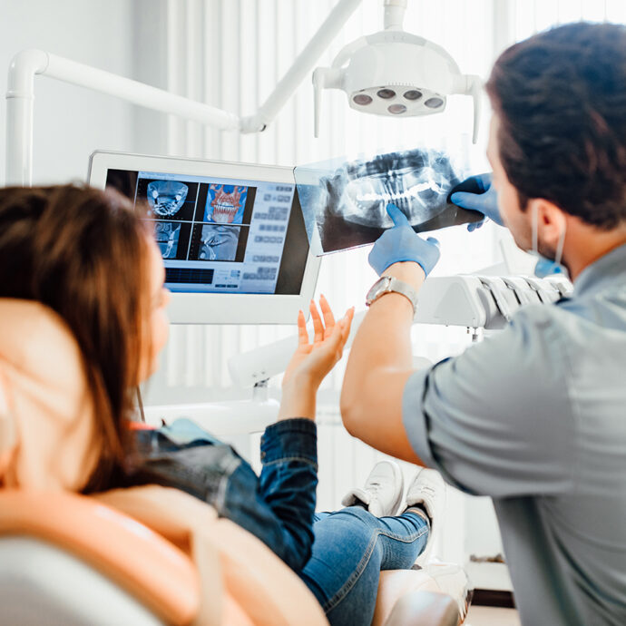 Medicine, dentistry and healthcare concept, male dentist showing teeth x-ray to female patient at dental clinic office.