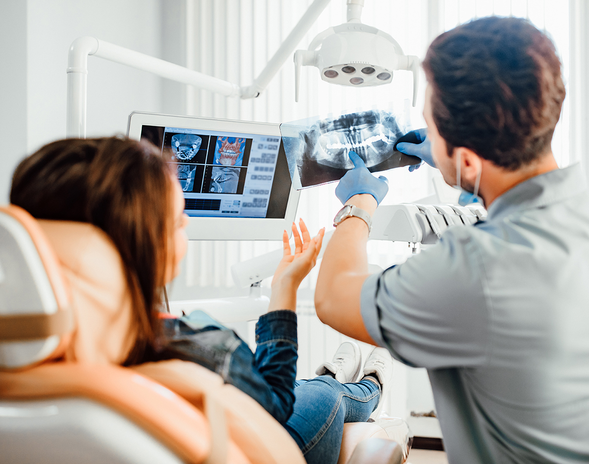 Medicine, dentistry and healthcare concept, male dentist showing teeth x-ray to female patient at dental clinic office.