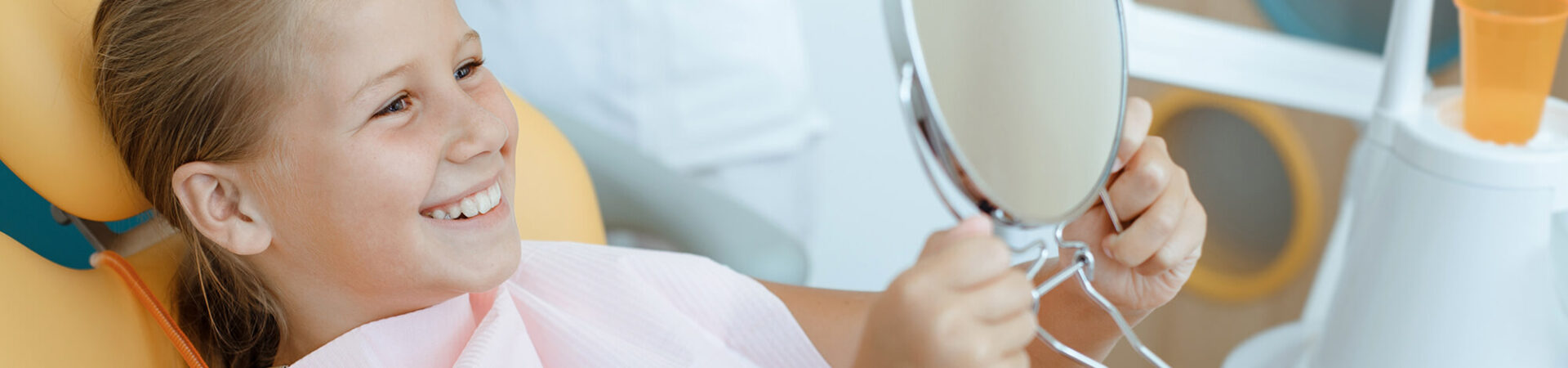 smiling girl sitting in a dentist chair looking at her teeth in the mirror