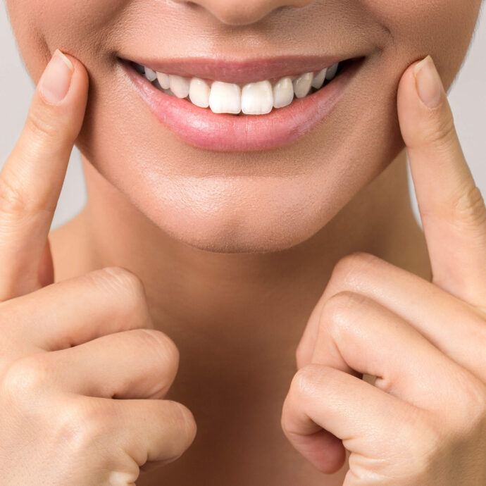 close-up of a person smiling and pointing at their white teeth
