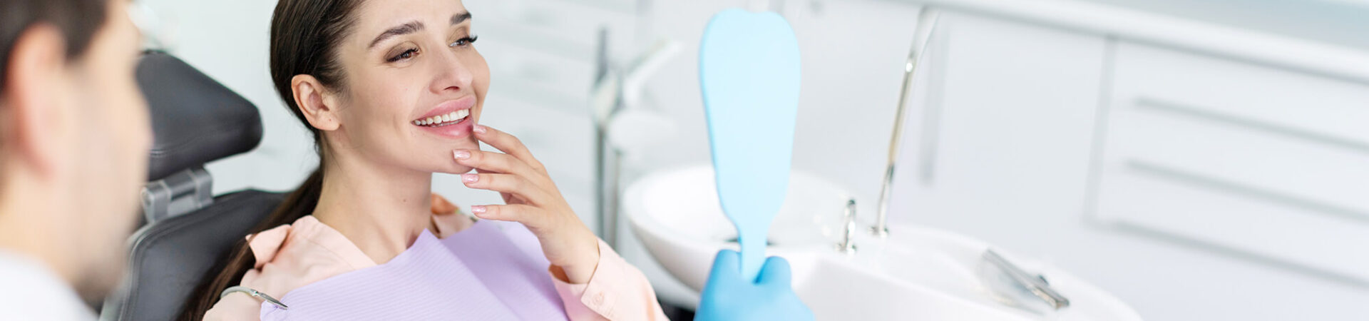 female sitting in dentist chair looking in the mirror at her teeth