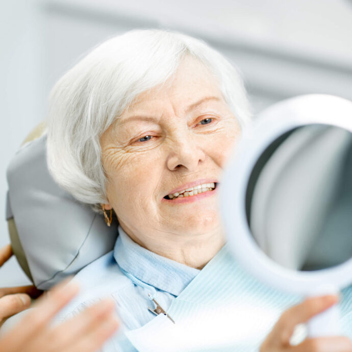 older female sitting in a dentist chair smiling and looking in the mirror at her teeth