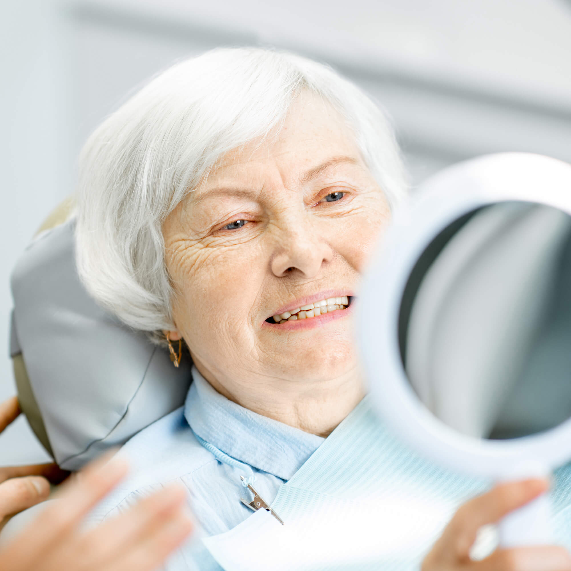 older female sitting in a dentist chair smiling and looking in the mirror at her teeth