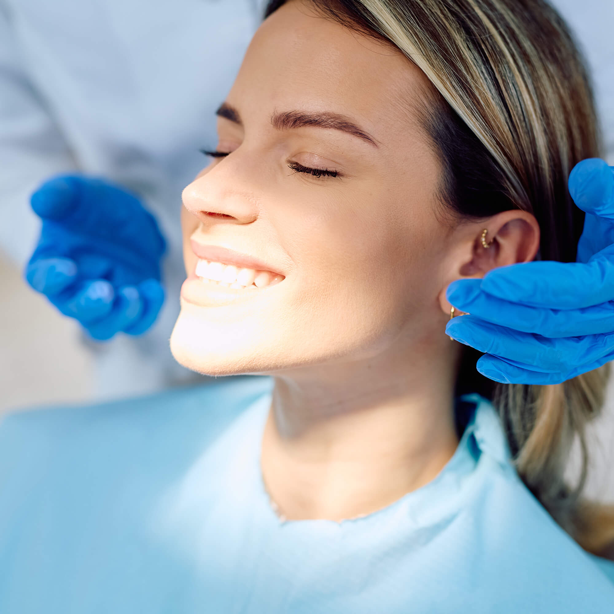 female sitting in dentist chair with eyes closed, smiling